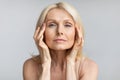 Antiage skincare. Senior woman touching skin near eyes and looking at camera, lady with flawless skin, grey background