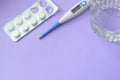 Antibiotic pills, thermometer and glass of water on purple background. Copy space for text. Take medicine and cold treatment conce Royalty Free Stock Photo