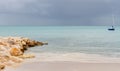 Antigua beach and rock jetty with sail boat and storm clouds on calm sea, tranquil and calming Royalty Free Stock Photo