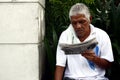 Adult or senior Filipino man relax and sit on a park bench and read newspaper