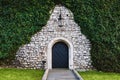 Antique arched wrought-iron doors in an old stone fortress wall using green lush ivy. Beautiful antique frnar over the old door Royalty Free Stock Photo