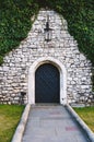 Antique arched wrought-iron doors in an old stone fortress wall using green lush ivy. Beautiful antique frnar over the old door Royalty Free Stock Photo