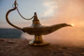 Antique artisanal Aladdin Arabian nights genie style oil lamp with soft light white smoke. Sunset mountain background Royalty Free Stock Photo