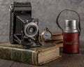 Antique bellows camera on an antique book with a thermos of coffee and a pocket watch next to it Royalty Free Stock Photo