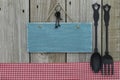 Antique blank blue sign with iron keys, gingham tablecloth and cast iron spoon and fork hanging on wooden background