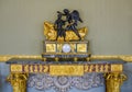 An antique clock decorated with golden bas-reliefs from ancient life and with a mythological sculpture at the top