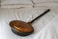 Antique copper bed warmer laying on white bed sheets. Copper and brass bed warmer