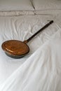 Antique copper bed warmer laying on white sheets. Copper and brass bed warmer