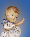 Antique cracked and worn baby doll in blue and white crochet dress against blue background Royalty Free Stock Photo