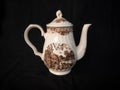 Antique cream ceramic teapot with a rustic motif on a black background