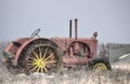 Antique faded red tractor sitting on dead grass with snow falling.