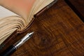 An antique fountain pen close-up next to an open book on a wooden textured table Royalty Free Stock Photo