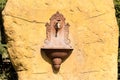 Antique French ornate wall fountain lavabo or planter with scrolling details and accents mounted in a stone block outside. A tap i