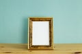 Antique golden picture frame on wooden table with mint green background