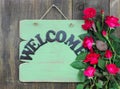 Antique green welcome sign with flower border of red roses hanging on rustic wood background