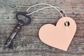 An antique handmade key with a heart-shaped label keychain lies on a wooden Board