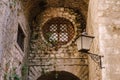 Antique hanging lantern in the wall of an old building with a window behind a round metal grate.