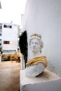 Antique head bust of woman against gray wall. Historical statue in golden dress himation. Ancient female face on light Royalty Free Stock Photo