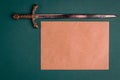 Antique knightly sword and a sheet of old paper on a green velvet background.