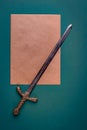 Antique knightly sword and a sheet of old paper on a green velvet background.