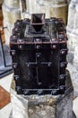 Antique metal forged box for collecting donations in the Christian church. It is painted black and mounted on a stone platform