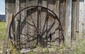 An antique metal wheel leaning against the wall of an abandoned wood building Royalty Free Stock Photo