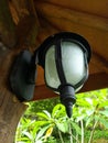 Antique and minimalist garden lamp with white mirror and black stalk attached to a wooden pole. Low angle and side view