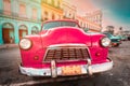 Antique pink car inext to colorful buildings in Old Havana