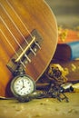 An antique pocket watch leaned against a ukulele and old book with vintage map and brass pen placed on wooden table. Royalty Free Stock Photo