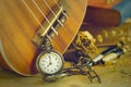 An antique pocket watch leaned against a ukulele and old book with vintage map and brass pen placed on wooden table.