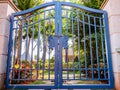 Antique steel blue double gate with padlock in front of a tropical garden