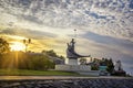 Antique stylized statue of spearman in boat on city embankment at sunset