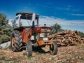 Antique tractor in front of a pile of cut logs against a cloudy blue sky