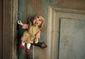 An Antique Traditional Puppet Laughing And Sitting On The Handle Of The Very Old Door