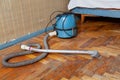 Blue vacuum cleaner stands on old parquet floor