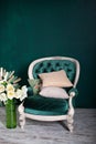 Antique velvet green armchair with a vase and bouquet of flowers near emerald wall. armchair on green background. Vintage