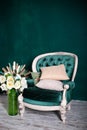 Antique velvet green armchair with a vase and bouquet of flowers near emerald wall. armchair Isolated on green background. Vintage