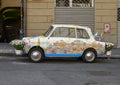 Antique white car with paintings of Genoa, flags of Genoa, and flower pots.