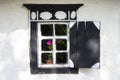 An antique window with rounded glass in a rectangular black frame with wooden shutters on the clay of a white clay wall