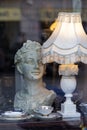 Antique woman bust sculpture near vintage lamp in shop window.