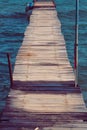 Antique wooden boardwalk over blue and azure sea. Small waves with calm sea. Some boats in the distance. On the boardwalk some
