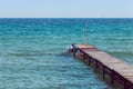 Antique wooden boardwalk over blue and azure sea. Small waves with calm sea. Some boats in the distance. On the boardwalk some