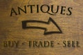 Antiques Buy Trade Sell sign set on a wood background and a right facing arrow. Brown 3D text against wood grain background.