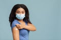 Antiviral immunization. Black lady vaccinated against covid-19, showing arm with plaster, standing on blue background Royalty Free Stock Photo