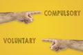 Antonym concept. Hands pointing to different sides. Voluntary or compulsory on yellow background.