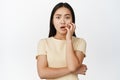 Anxious asian girl biting fingernails and looking worried, being in trouble, panicking, standing over white background