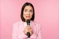 Anxious asian lady in suit, talking in public, giving speech with microphone on conference, looking scared, standing