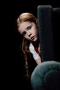 Child looking at camera while hiding behind armchair on black