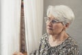 anxious concerned elderly caucasian pensioner wearing glasses and looking uneasily through the window Royalty Free Stock Photo
