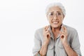 Anxious and concerned hopeful silly senior woman in glasses with white hair crossing fingers for good luck frowning